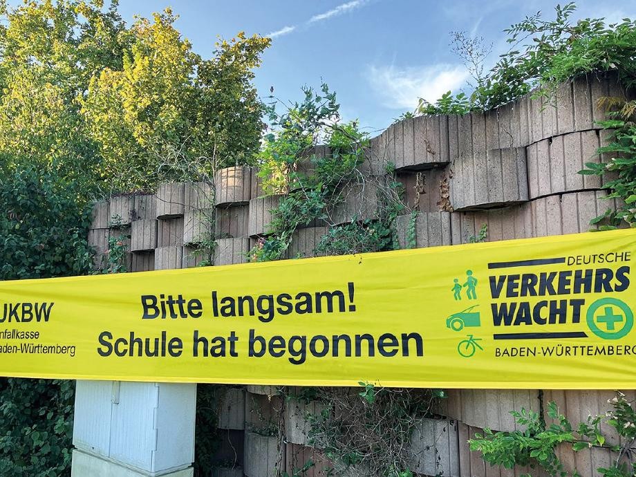 Schulstart Mauer am Straßenrand mit einem gelben Banner und der Aufschrift: Bitte langsam, Schule hat begonnen.