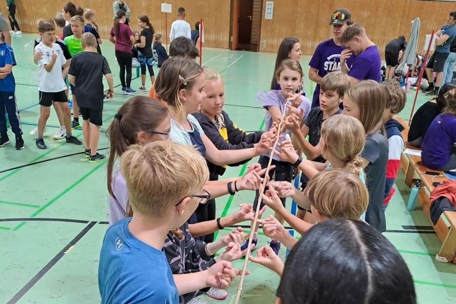 Kinder stehen in einer Turnhalle nebeneinander und spielen ein Spiel mit einem Band.