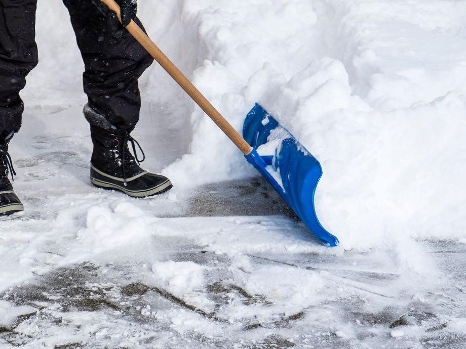 Winterdienst Eine Person schippt mit einer blauen Schneeschaufel Schnee.